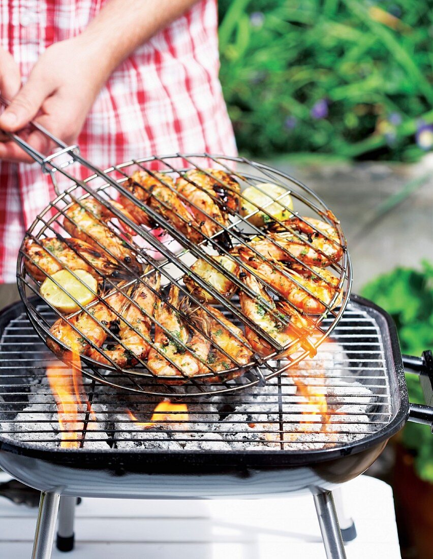 Marinierte Riesengarnelen in Grillgitter werden gewendet auf Grill