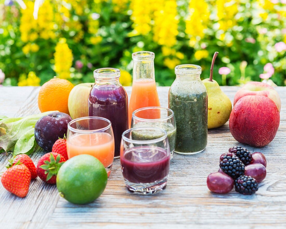 Verschiedene Smoothies in Gläsern und Flaschen mit Früchten und Salat