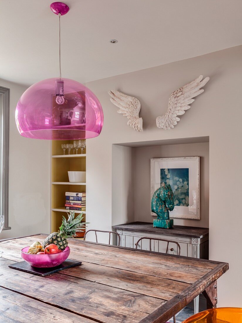 Rustic iron table with wooden top below pink pendant lamp and artwork on top of sideboard in niche