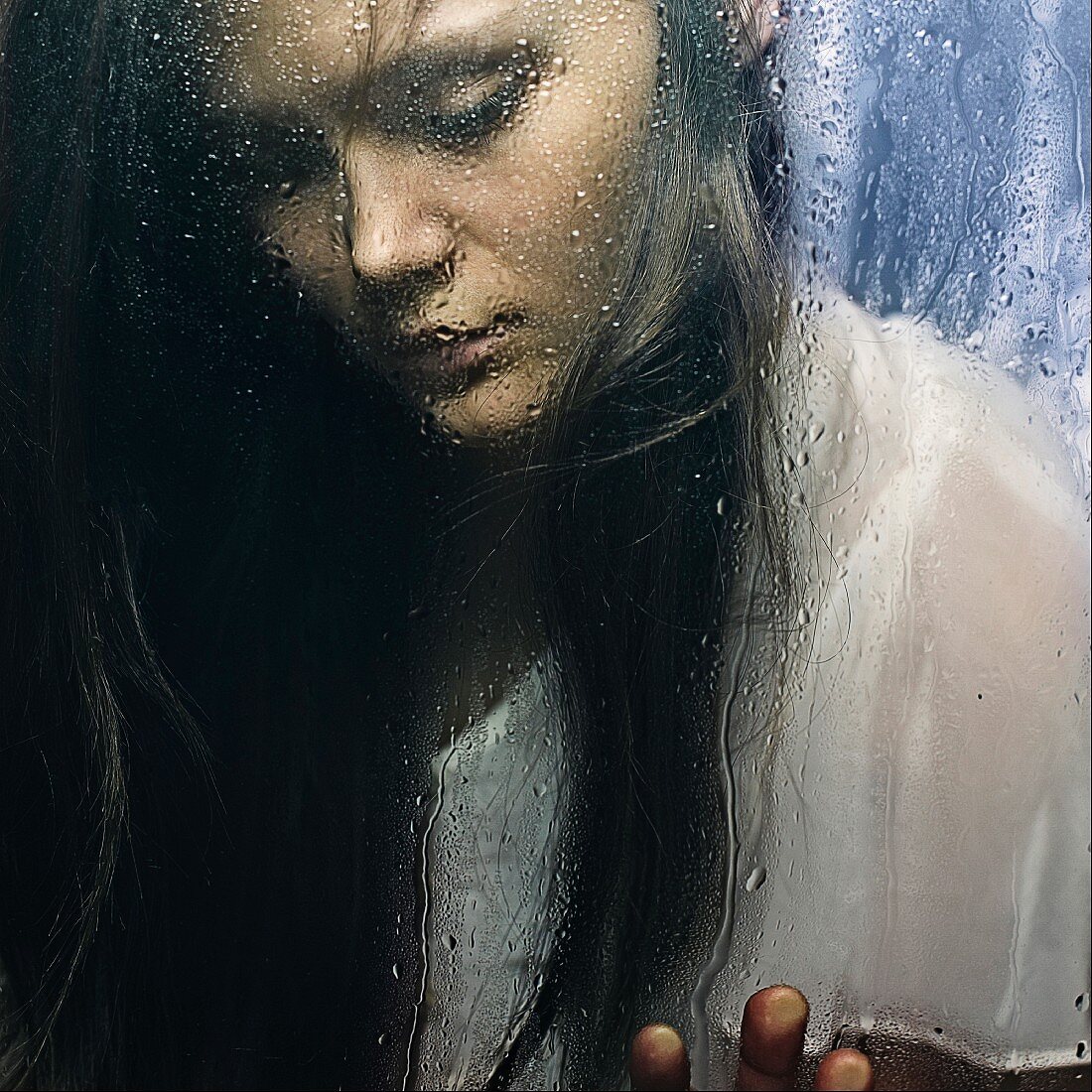 A young, depressed-looking woman behind a wet glass panel