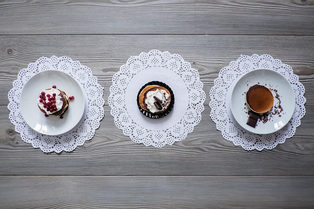 Drei verschiedene Desserttörtchen auf Papierspitzendeckchen (Aufsicht)