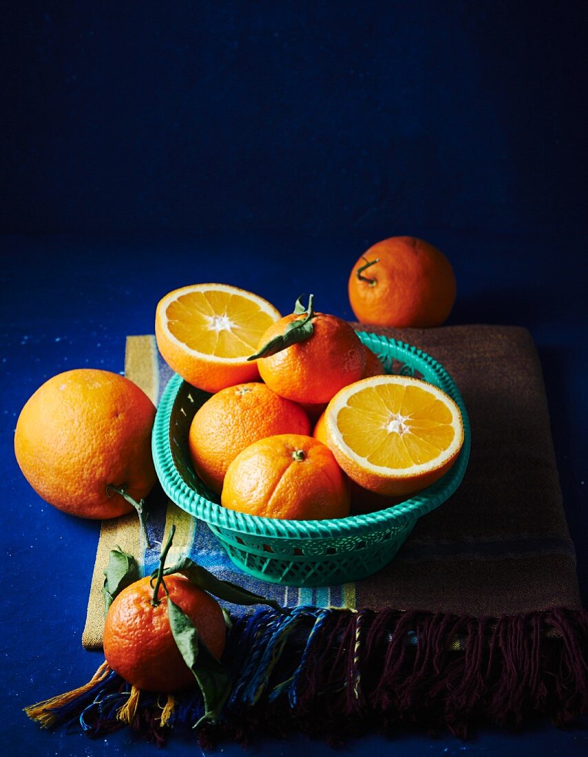 Orangen, ganz und halbiert, im Korb und daneben