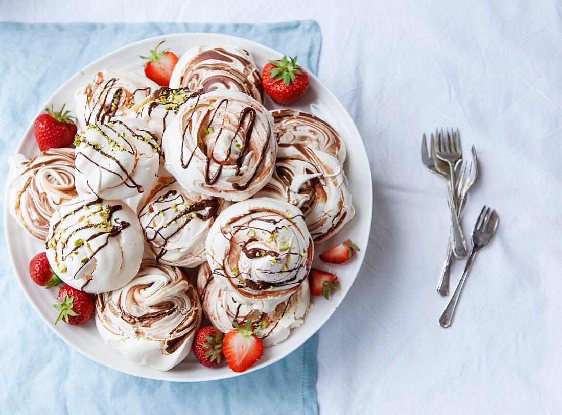 Various meringues with chocolate sauce, strawberries and pistachio nuts on a plate (seen from above)