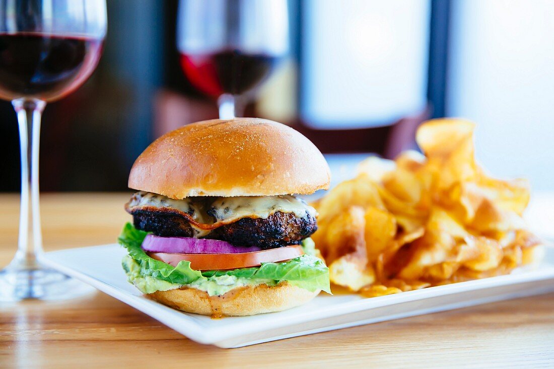 Cheeseburger mit Kartoffelchips und Rotwein auf Restauranttisch