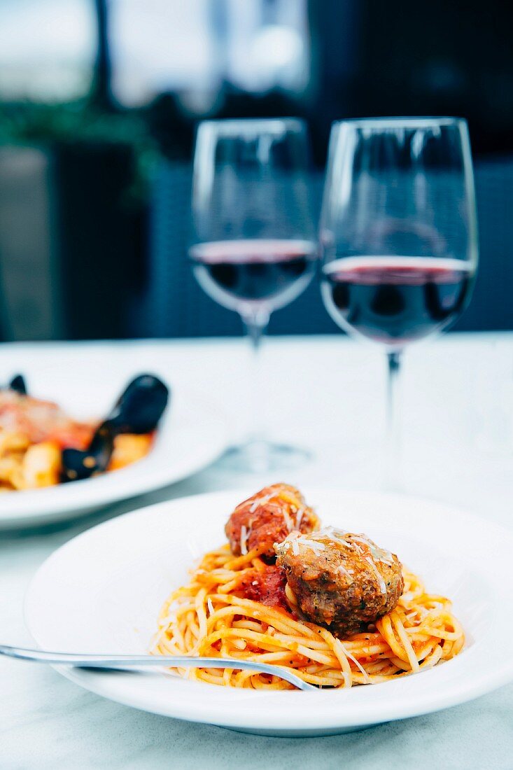 Pasta with meatballs, a seafood platter and two glasses of wine on the table