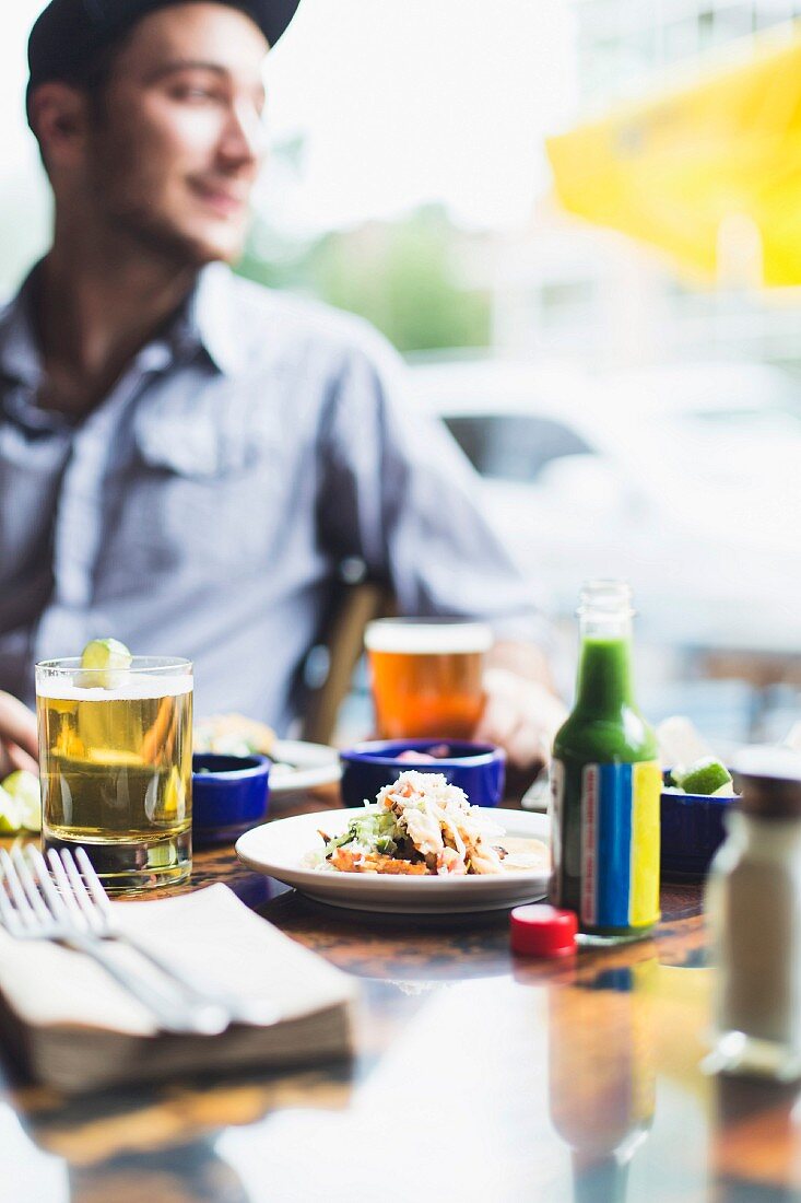 A young man sitting at a restaurant table with beer and food