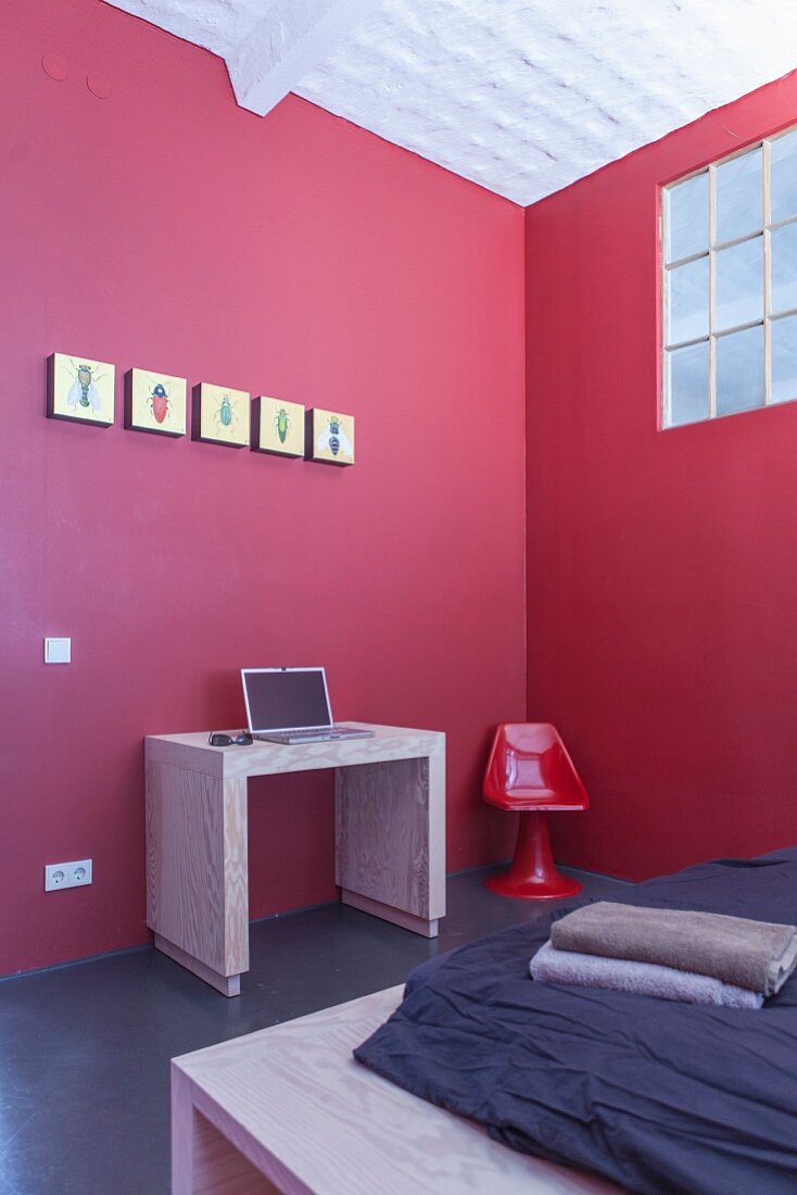 Minimalistischer Schreibtischplatz mit Laptop an roter Wand in Schlafzimmer mit Industrieverglasung