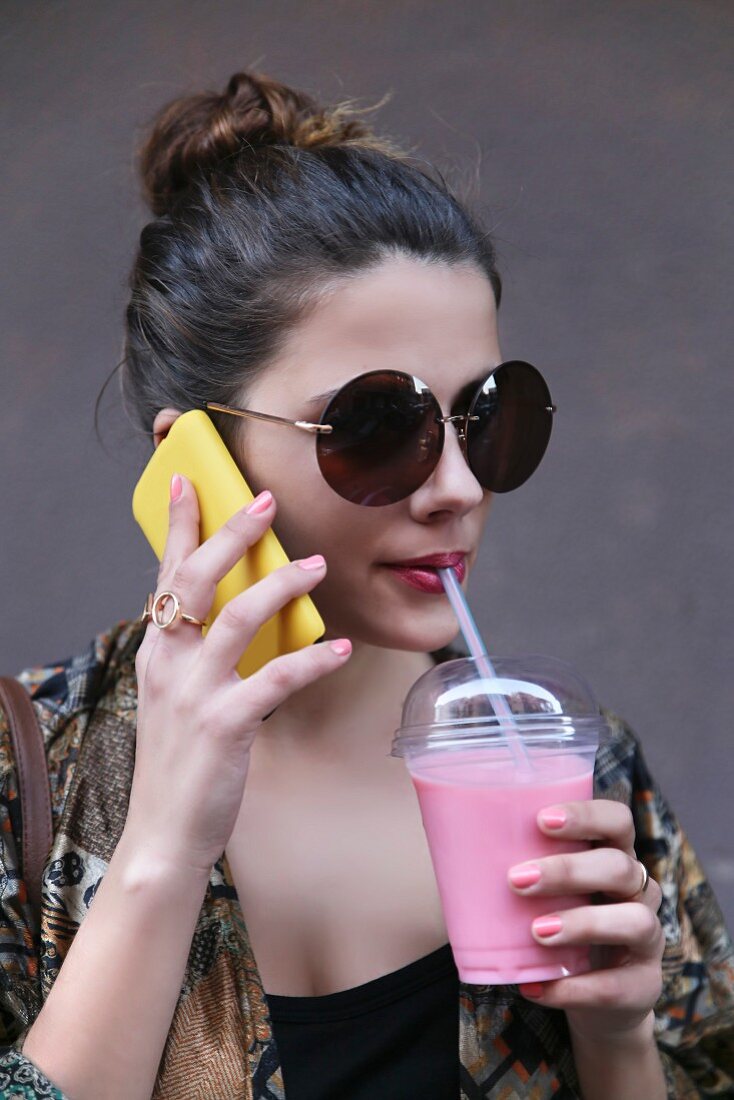 Young woman drinking a smoothie while talking on a smartphone