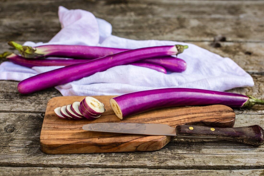 Aubergines, whole and slices, on a wooden board