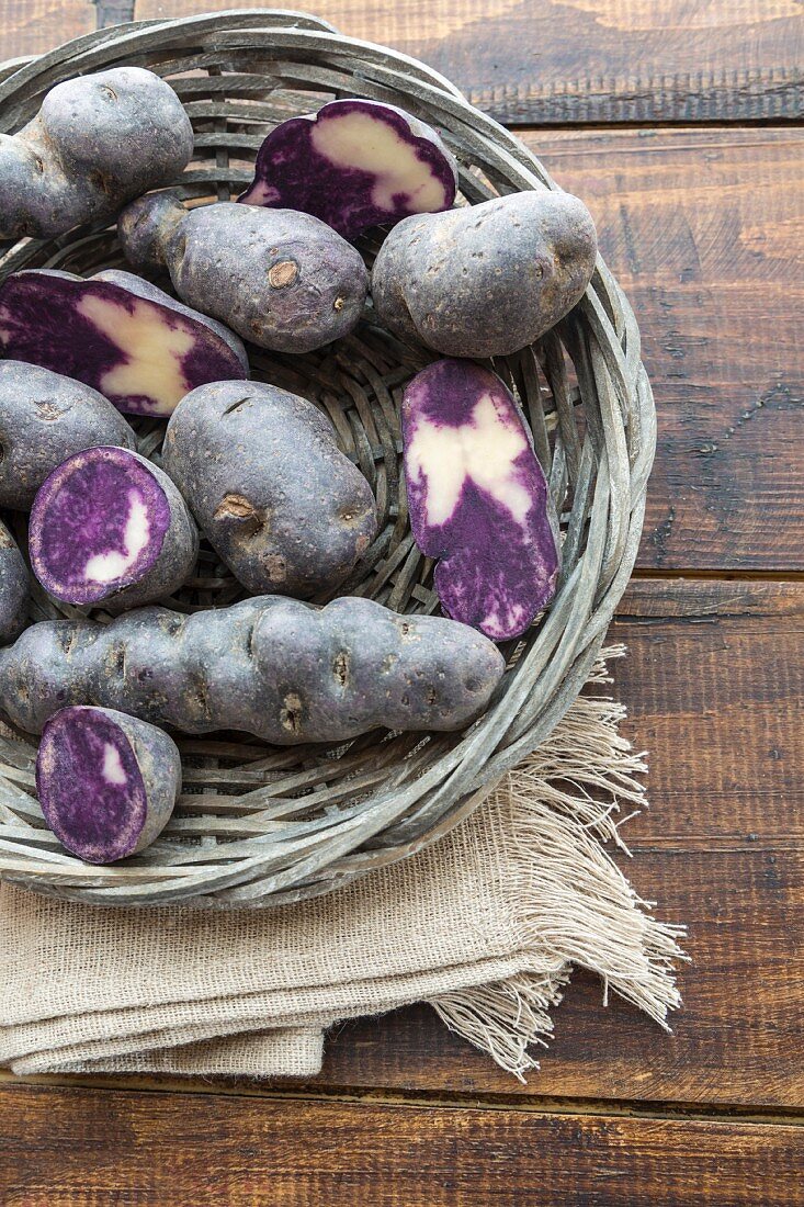 Purple potatoes, whole and halved, in a wicker basket
