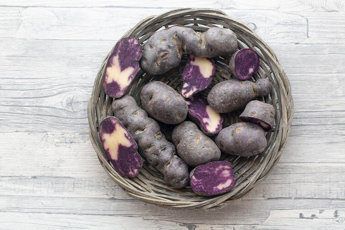 Purple potatoes, whole and halved, in a wicker basket (seen from above)