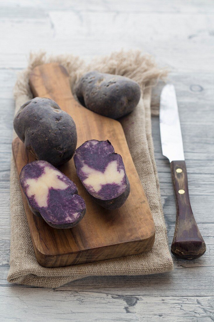 Violette Kartoffeln, ganz und halbiert auf Holzbrett