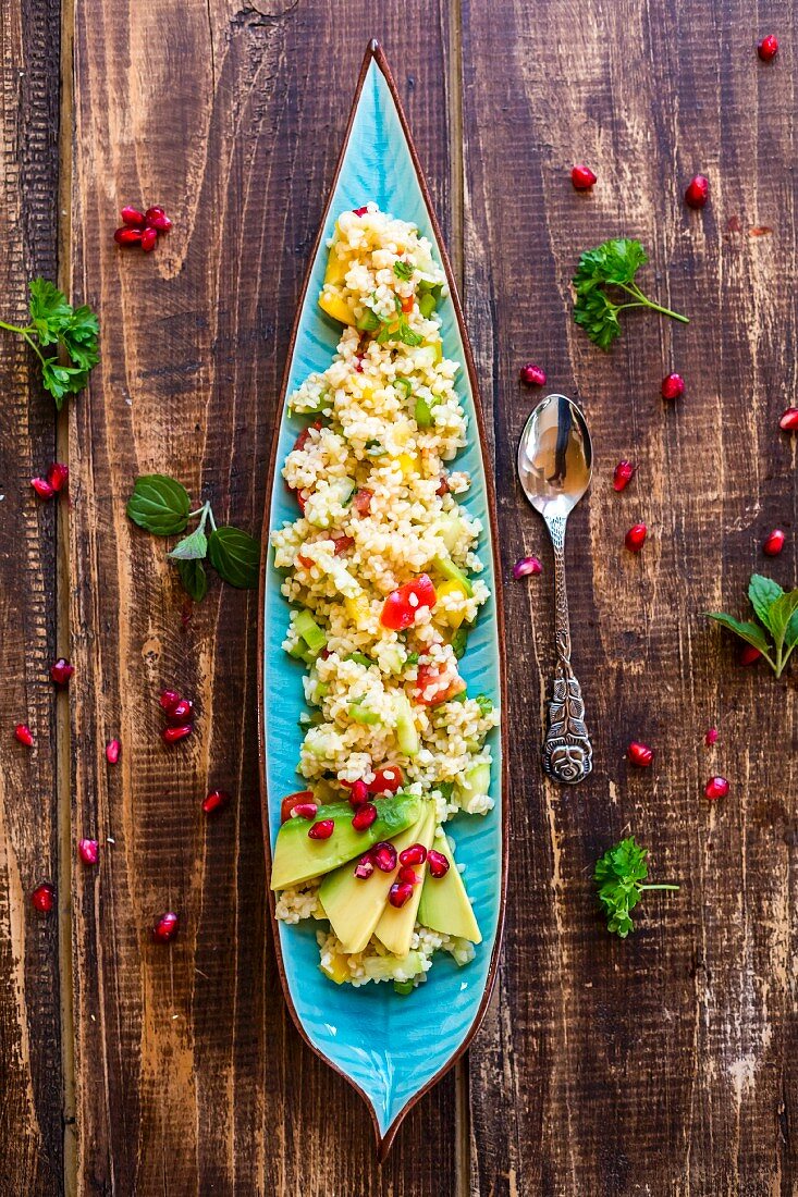 Vegan bulgur salad with vegetables, avocado and pomegranate seeds (seen from above)