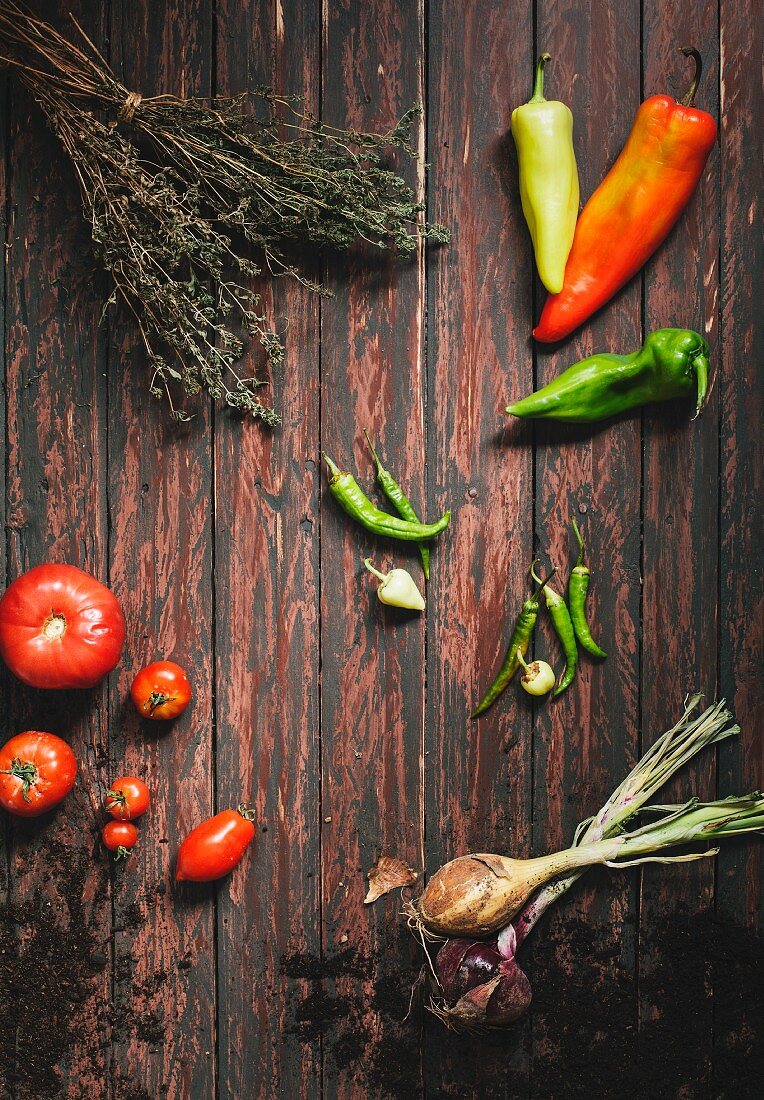 Spitzpaprika, Chilischoten, Tomaten, Zwiebeln und Bohnenkraut auf Holzuntergrund
