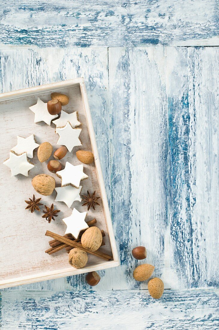 Cinnamon stars, cinnamon sticks, star anise and nuts in a wooden crate (seen from above)