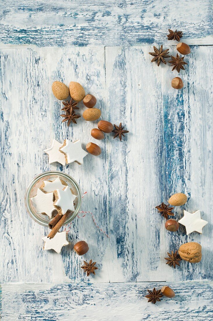 Cinnamon stars, cinnamon sticks, star anise and nuts on a wooden surface (seen from above)