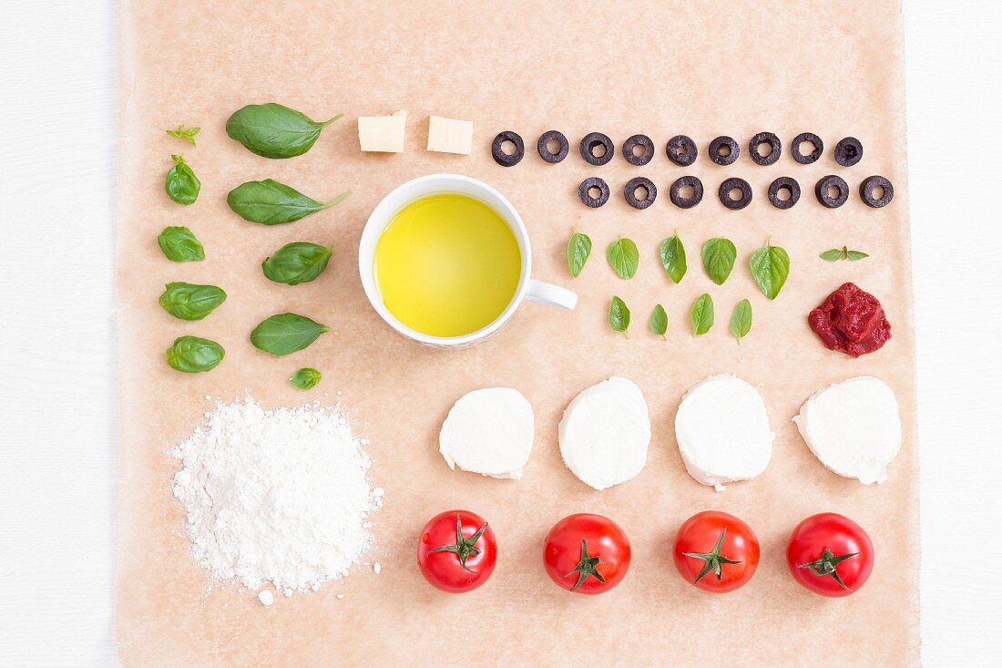 Rows of various pizza ingredients on a piece of baking paper