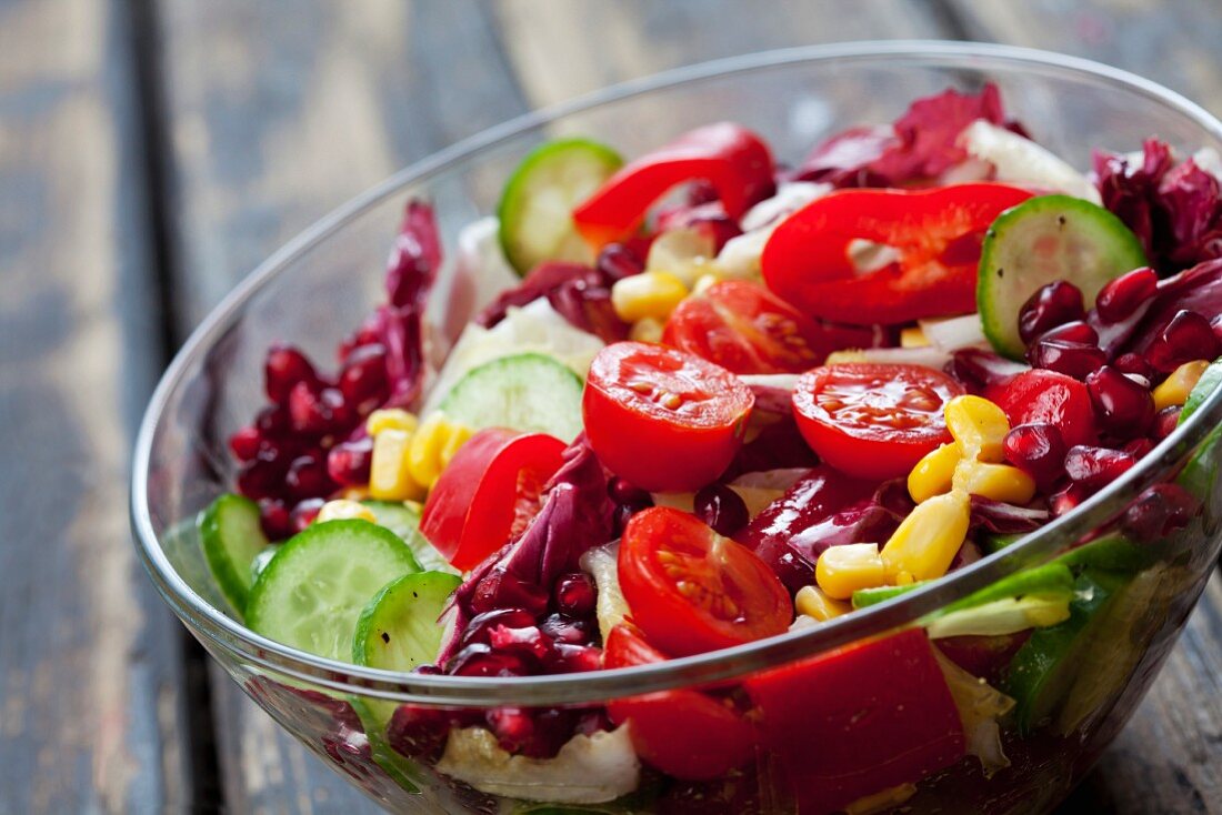 A mixed vegetable salad with pomegranate seeds in a glass bowl