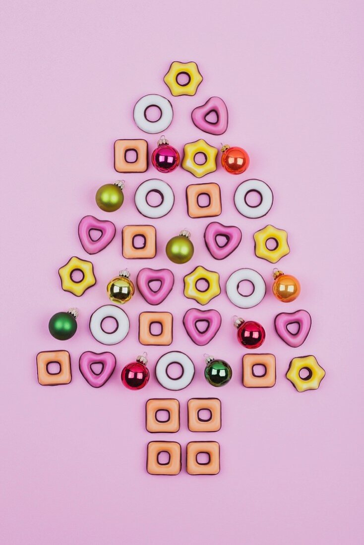 Christmas cookies and baubles on a pink surface in the shape of a Christmas tree