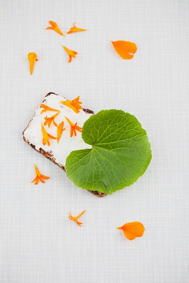Slice of bread topped with cream cheese, and wasabi leaf and marigold petals
