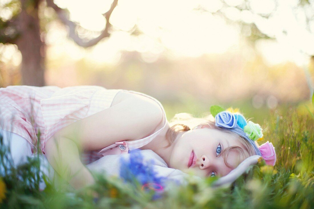 A little girl wearing a dress and a floral headband lying in the grass