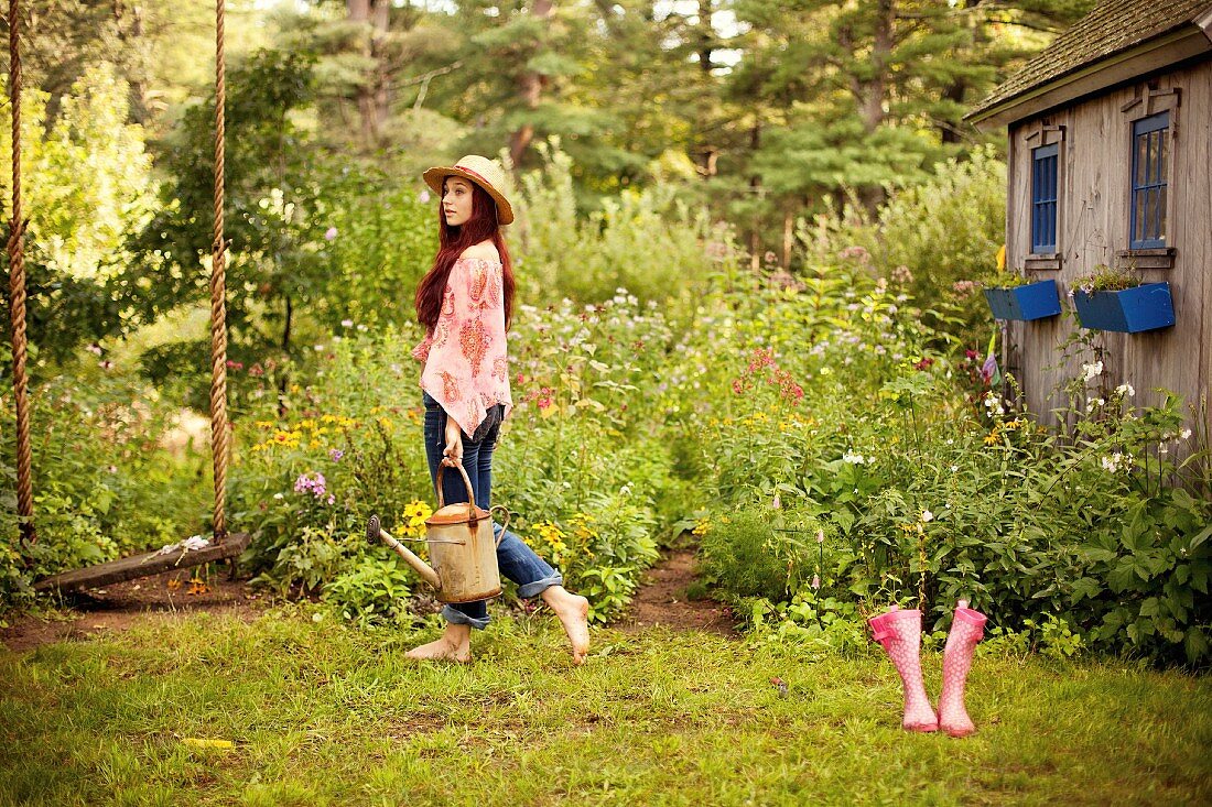 Junge Frau im Hippielook mit Gießkanne im Garten