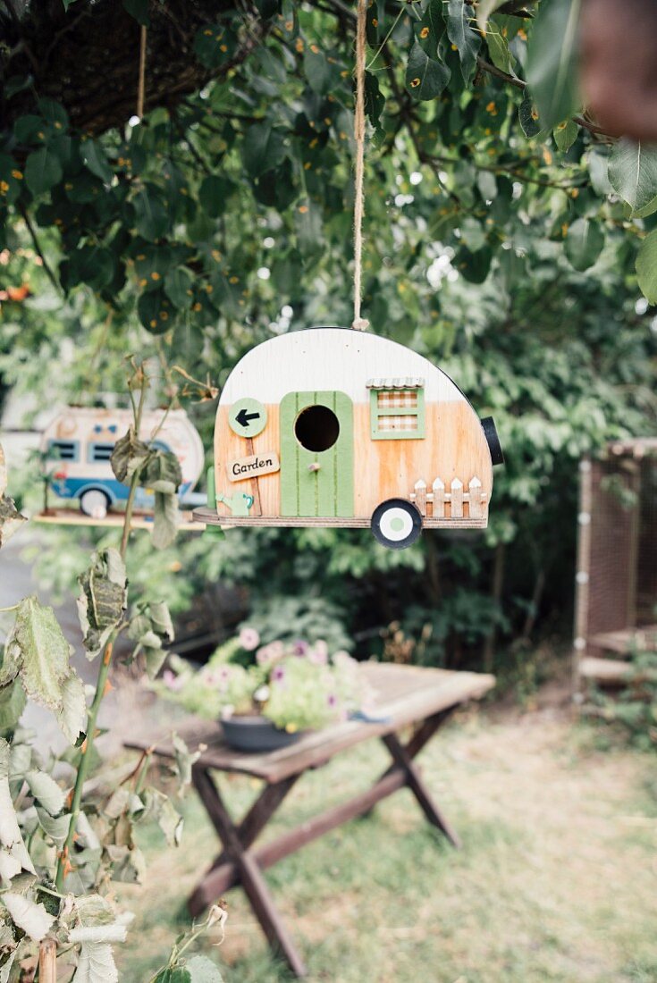 Caravan-shaped bird nesting box hanging in a tree