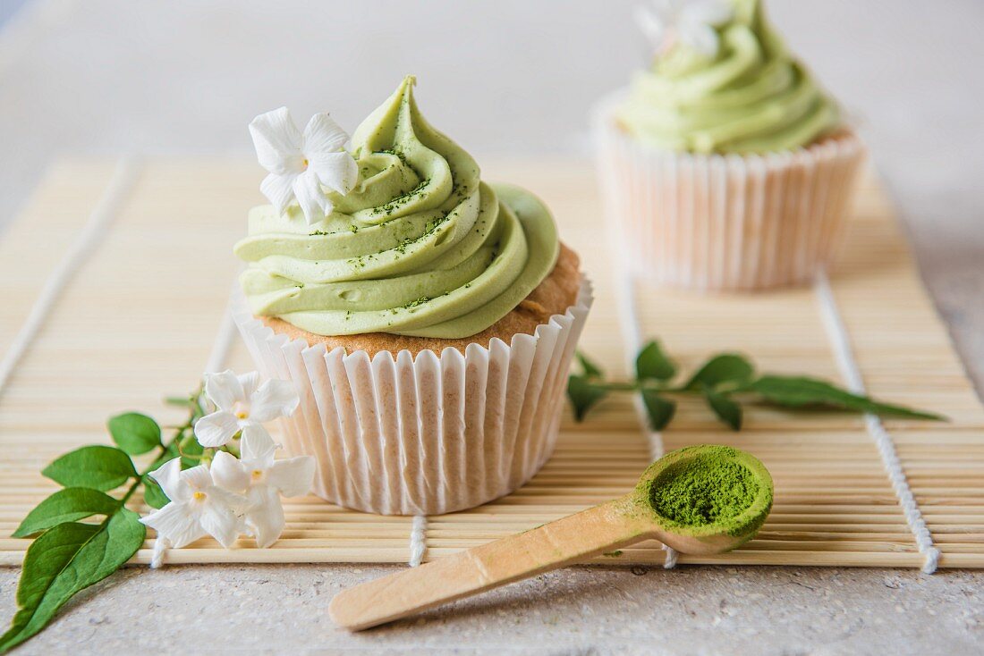 Matcha cupcakes with jasmine flowers and matcha powder on a wooden spoon