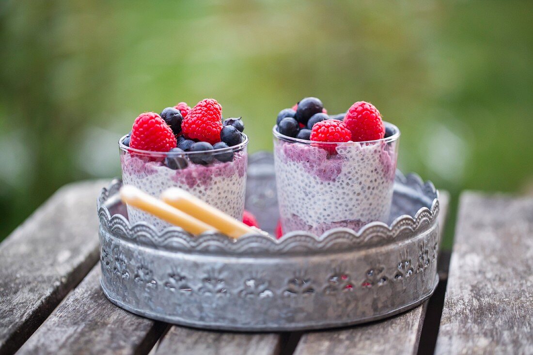 Two glasses of chia pudding with blueberries and raspberries on a metal tray