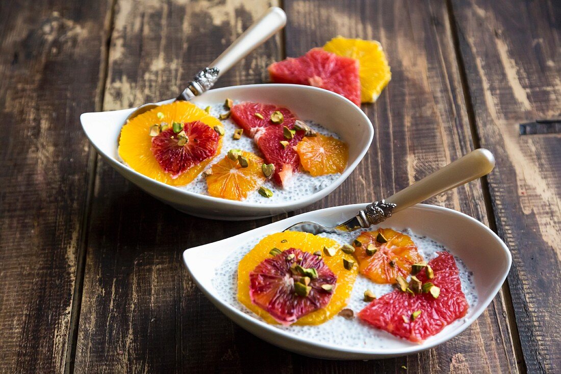 Chia-Pudding mit Orangen- und Grapefruitscheiben in Schälchen auf Holzuntergrund