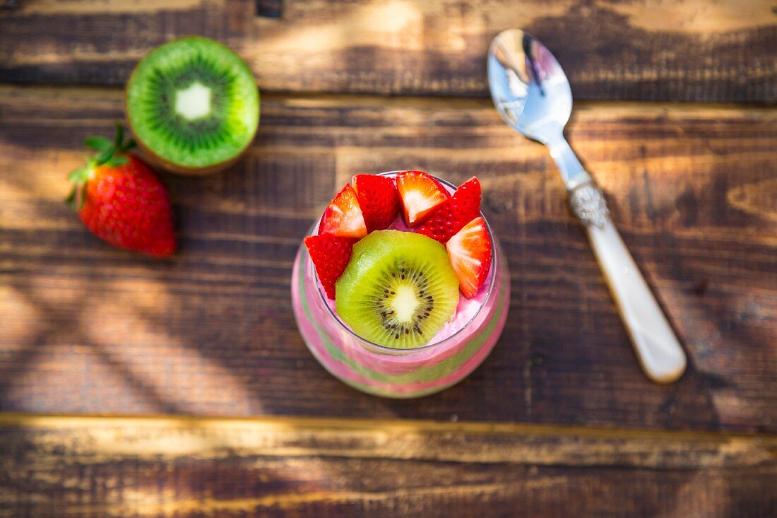 Chia-Pudding mit Kiwi und Erdbeeren im Glas auf Tisch im Freien