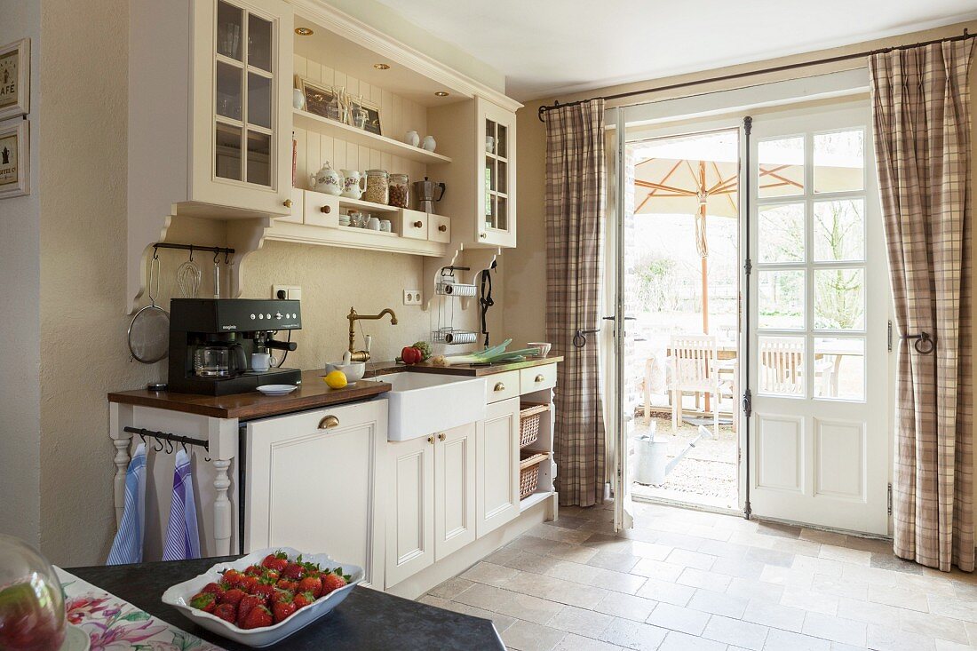 Vintage wall units in country-house kitchen with view onto sunny terrace through lattice windows