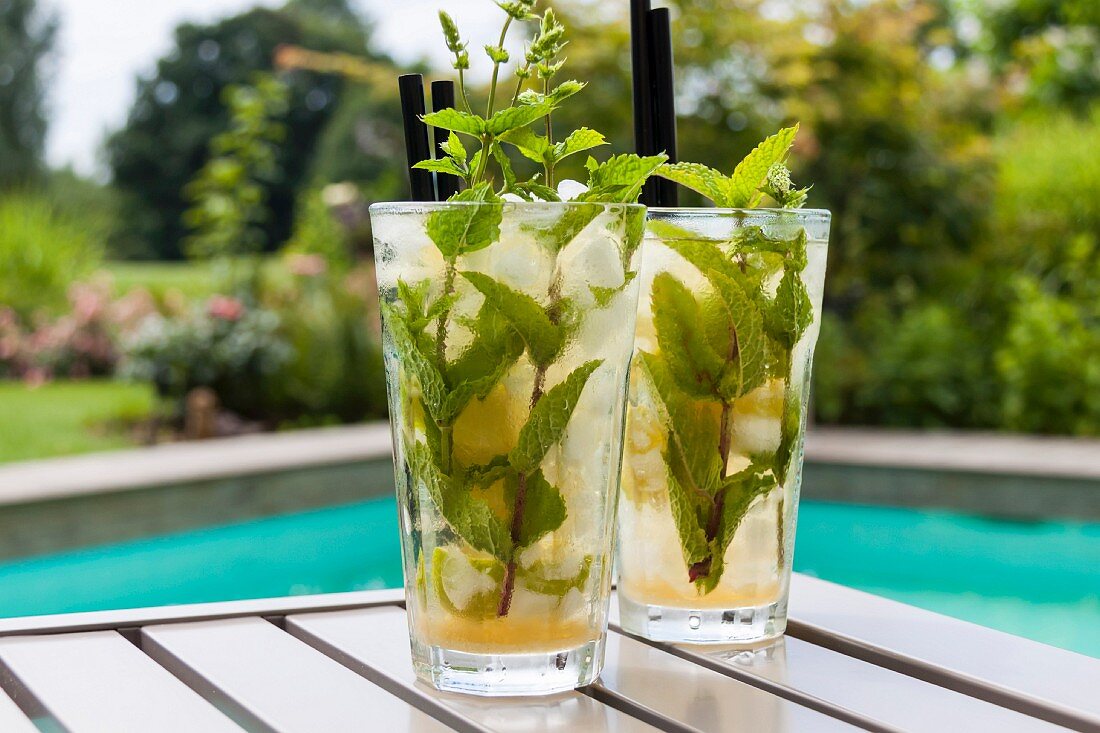 Two Mojitos on a table by a pool