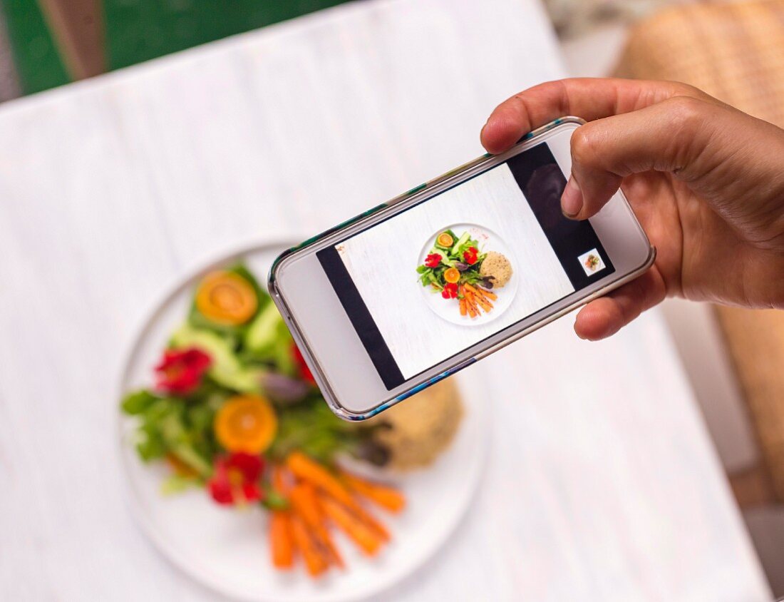 Frau fotographiert Gericht mit Quinoa und Salat auf Tisch mit Smartphone