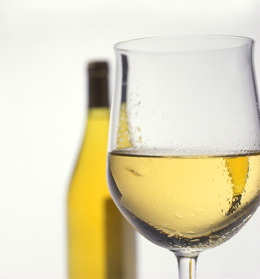 Gekühlter Weißwein im Glas, dahinter eine Flasche Weißwein