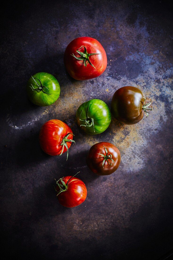 Various different coloured tomatoes on a dark surface (seen from above)