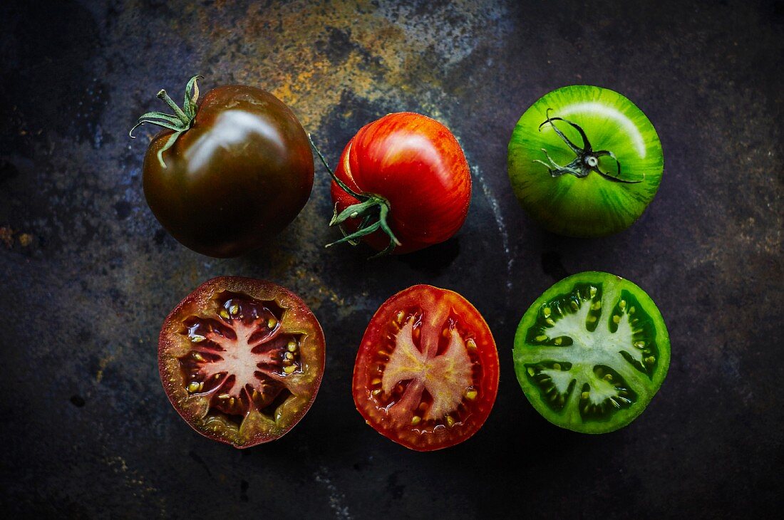 Black, red and green tomatoes and three halves (seen from above)