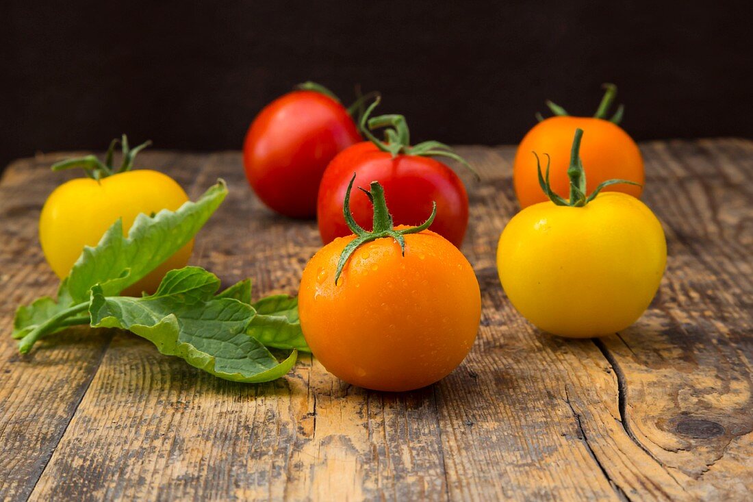 Orange, red and yellow tomatoes on a wooden surface