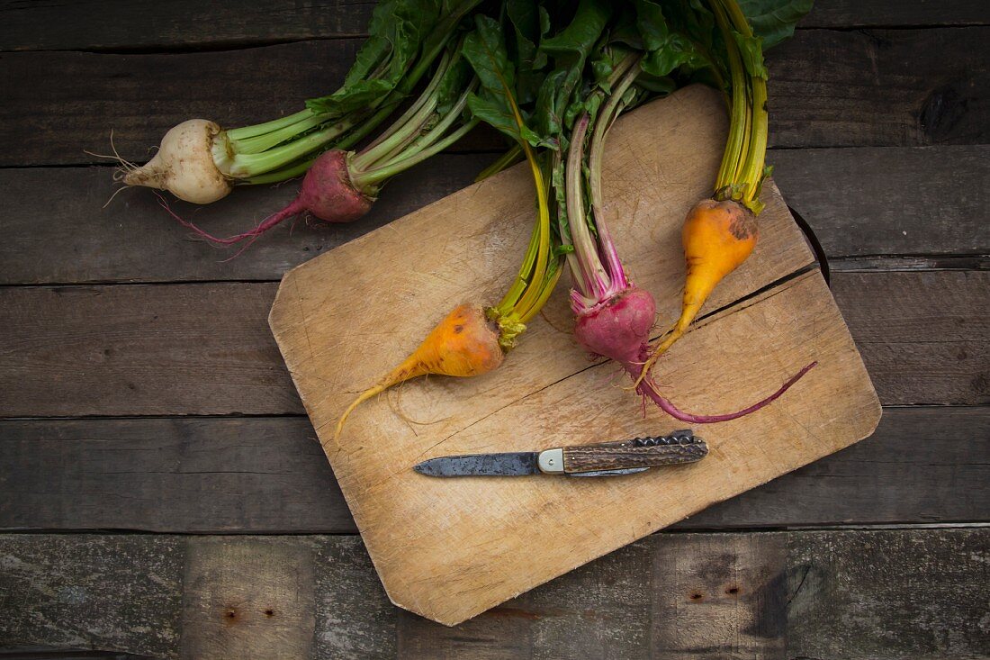 Red, white and yellow organic turnips on a wooden chopping board (seen from above)
