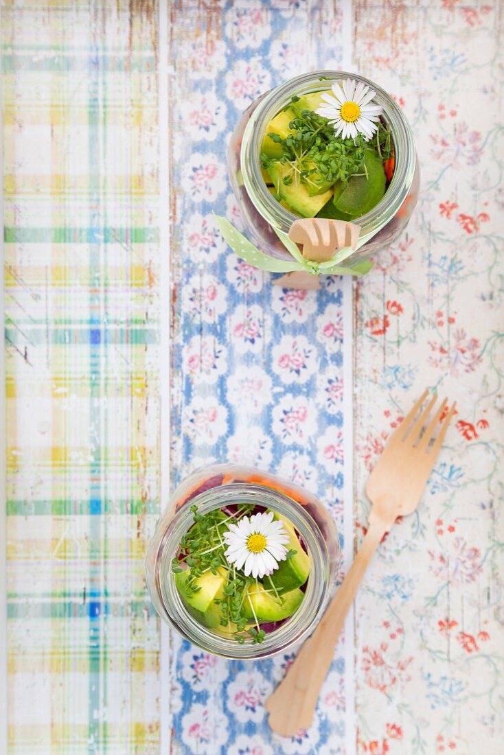 Frühlingshafter Schichtsalat mit Reis, Gemüse und Gänseblümchen in Gläsern