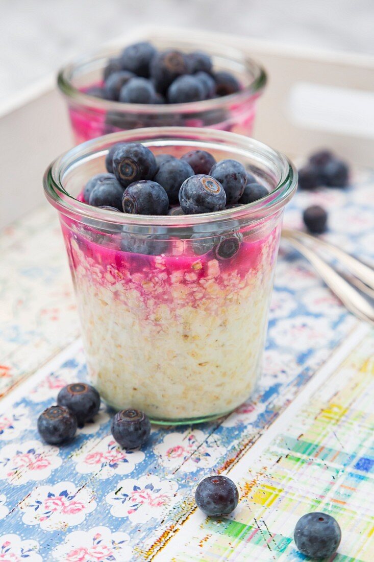 Glasses of overnight oats with blueberries and berry juice on a tray