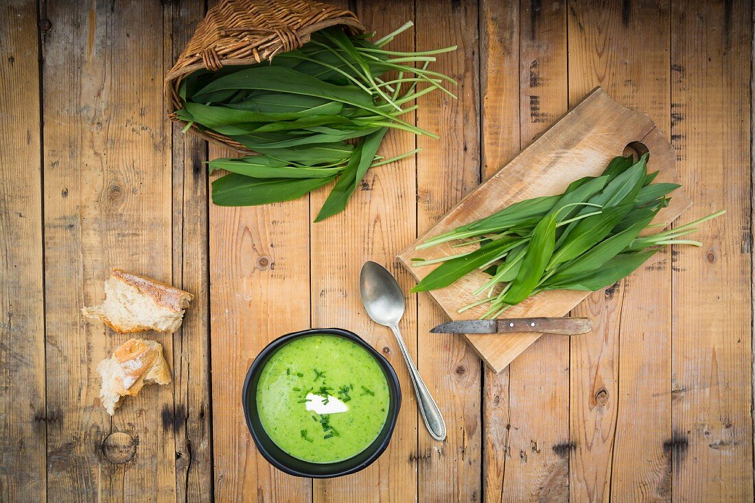 Cream of wild garlic soup and fresh wild garlic leaves on a wooden surface (seen from above)