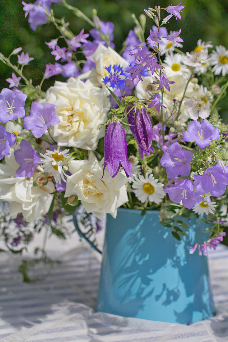 Blau-weißer Blumenstrauß in einer Emaillekanne auf dem Gartentisch