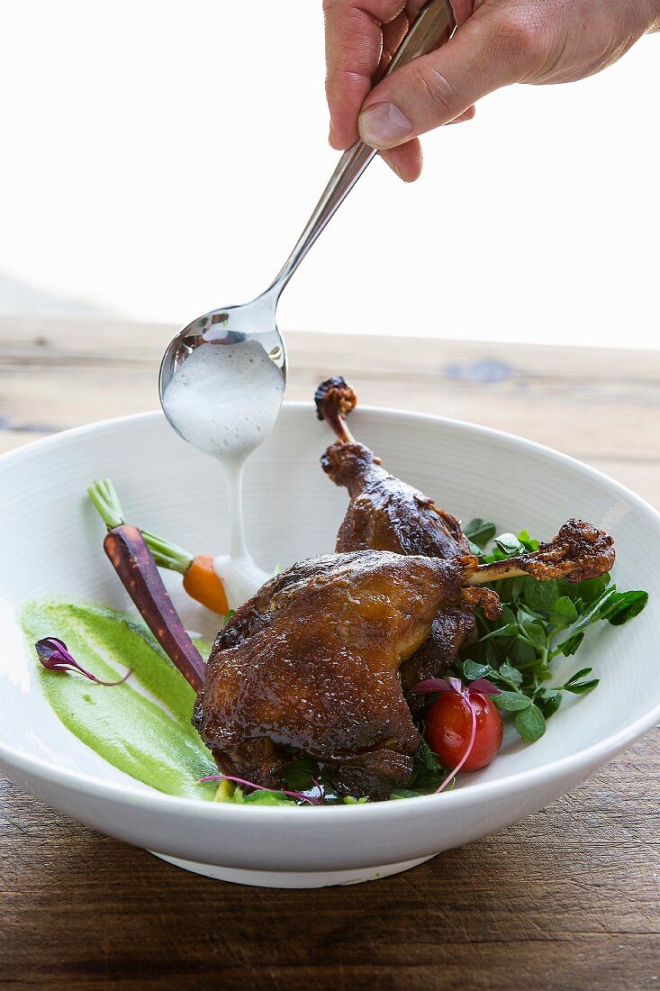 Side of vegetables with roasted duck leg being drizzled with sauce