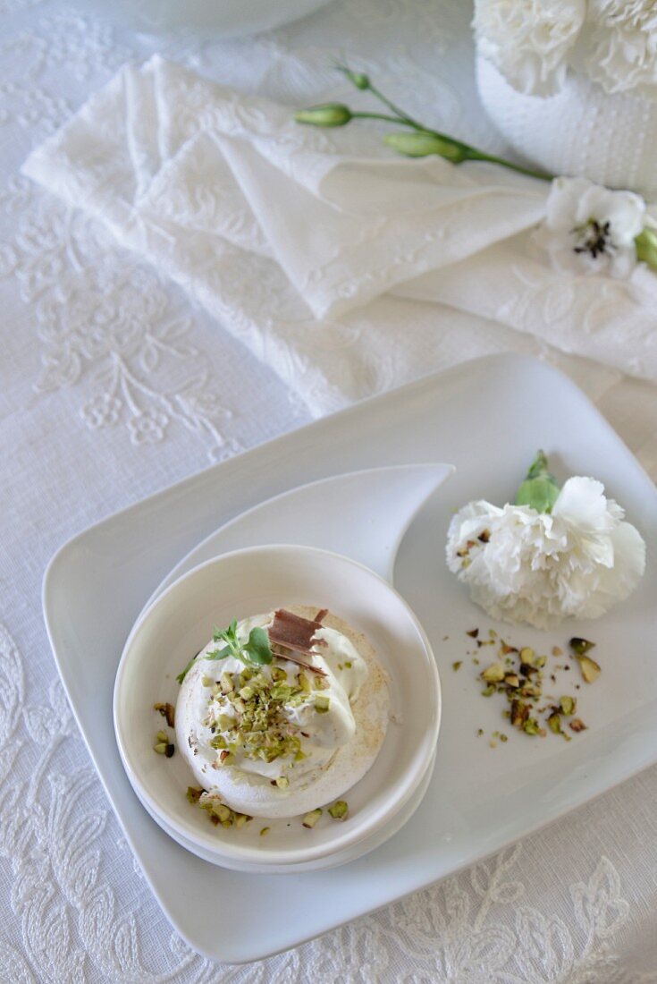 Mini pavlova with grated chocolate and chopped pistachio nuts next to decorative romantic flowers