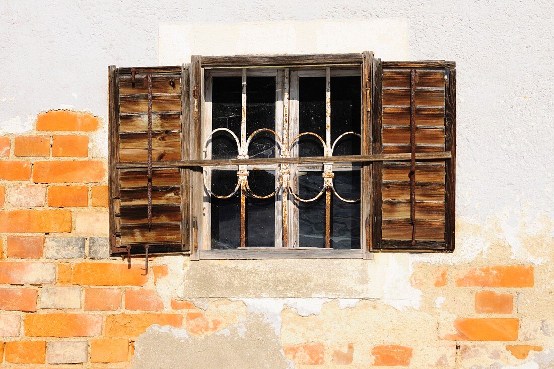 Old window with bars and shutters in façade wit crumbling plaster