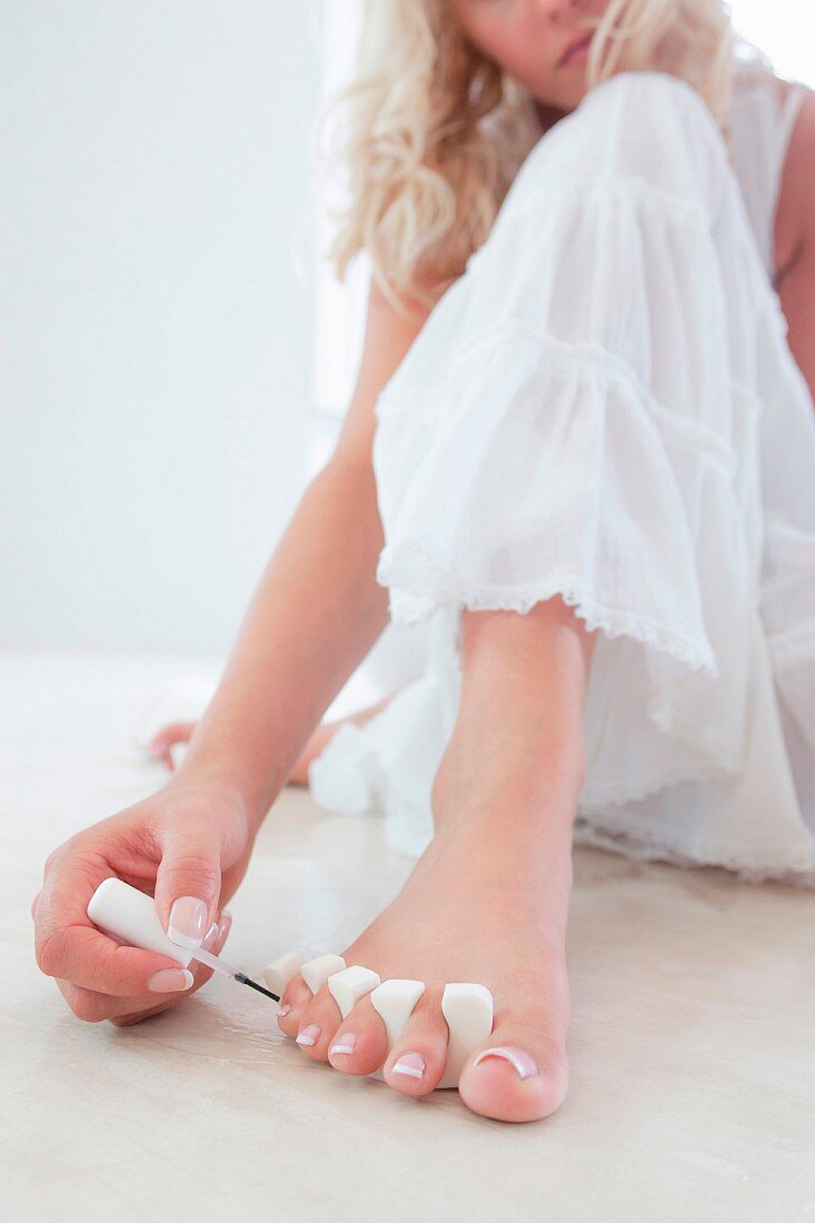 A young woman in a dress painting her toenails