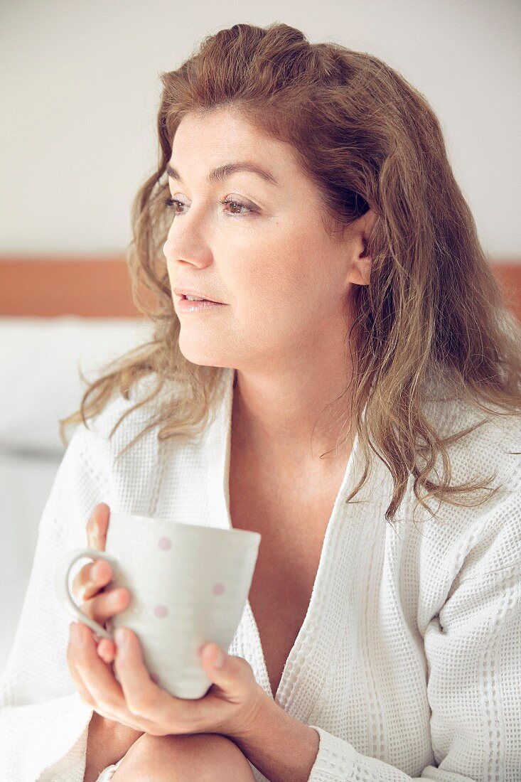 A middle-aged woman in a bathrobe holding a mug of coffee in her hand