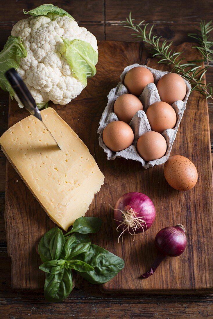 Zutatenstilleben mit Käse, Eiern, Blumenkohl, Kräuter und Zwiebeln