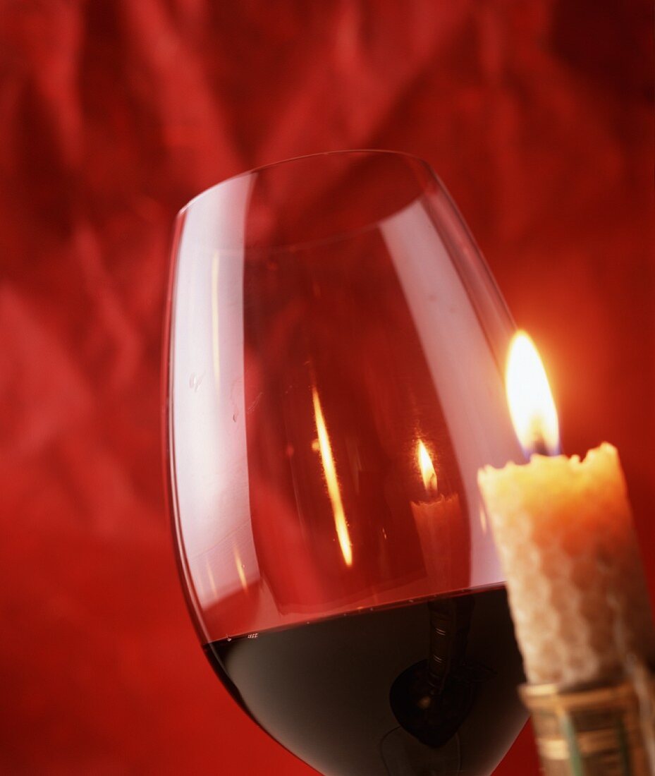 Ein Rotweinglas neben brennender Kerze vor rotem Hintergrund